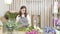 Young woman florist preparing flowers for creating a bouquet or composition, inspecting and pruning them in the workshop