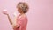 Young woman with flowers in curly hair holding piggy bank and doing magic with a finger for savings to grow