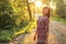 Young woman on forest path, looking down over her shoulder sun behind her, backlight creates nice bokeh in background