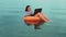 A young woman freelancer in an inflatable ring swims near the sea in the morning and works in a laptop