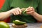 Young woman with fresh avocado at the table. The girl is cleaning a green avocado