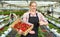 Young woman gardener in apron pholding crate with fresh strawberries