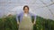 Young woman gardener putting on apron, ready for work at plant shop greenhouse