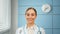Young woman general practitioner in white coat with blue stethoscope looks straight
