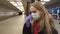 Young woman-girl in protective sterile medical face mask sitting on a bench and waiting for public transport on metro station, vir