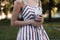 Young woman in a glamorous pink striped dress stands in the park with a sweet milkshake in her hands in a summer day.