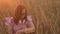 Young woman in glasses browsing smart watch, sitting in dry grass on sunset in windy weather.