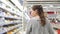 A young woman with glasses moves along open refrigerators at a grocery store.