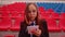 Young woman in glasses with notepad, pen talking on mobile phone, sitting on stadium bleachers. Female journalist