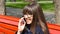 Young woman in glasses talking on the modile phone in a city park. Girl sitting on a red bench outdoor in spring and