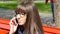 Young woman in glasses talking on the modile phone in a city park. Girl sitting on a red bench outdoor in spring and