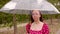 Young woman in glasses with transparent umbrella standing on street in strong wind, hurricane. Female in red dress