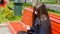 Young woman in glasses uses cell smartphone in a city park. Girl sitting on a red bench outdoor in spring and uses a