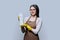 Young woman in gloves apron with organic detergent on gray background