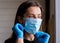 Young woman in gloves puts on a medical mask near the window at home