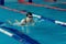 Young woman in goggles and cap swimming breaststroke stroke style in the blue water indoor race pool