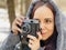 Young woman in gray coat photographing on old photo camera in forest. Pretty female taking photos with old camera in