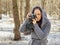 Young woman in gray coat photographing on old photo camera in forest. Pretty female taking photos with old camera in