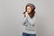 Young woman in gray sweater, hat and scarf with lowered head warming her hands isolated on grey background. Healthy