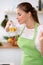 Young woman in the green apron cooking in the kitchen. Housewife smelling the oil while enjoys prepairing salad.