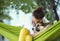 Young woman in green hammock with cute dog Welsh Corgi in a park outdoors. Beautiful happy female in white shirt