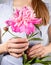 Young woman in grey T-shirt holding wonderful gentle pale pink peony close up. Image in trendy style without face