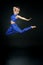 Young woman gymnast in blue suit jumping against a black background
