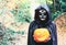 Young woman with halloween paint face mask wearing black hood - Scary witch holding spookey craved pumpkin