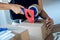 Young woman hands holding packing machine and sealing cardboard boxes with duct tape to delivery products ordered online to