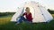 a young woman happily set up a tent on the mountain hills during sunset, for rest after a hike. woman drinking hot tea