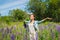 Young woman, happy, standing among the field of violet lupines, smiling, purple flowers. Blue sky on the background. Summer, with