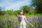Young woman, happy, standing among the field of violet lupines, smiling, purple flowers. Blue sky on the background. Summer, with