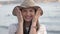 Young woman with hat covers and opens her eyes the she is surprised, sea background. Excited, funny and happy girl. Slow