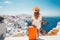 Young woman in hat with orange suitcase on Santorini island, Greece, Happy moment with young woman rear view tourist as orange the