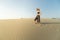 Young woman with hat walking in the desert dunes with footsteps in the sand during sunset