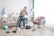 Young woman having back ache from cleaning after party chaos in her apartment, vacuuming floor, empty space