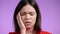 Young woman having headache, studio portrait. Girl putting hands on head, isolated on violet background. Concept of