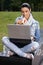 Young woman having lunch in park using laptop