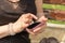 Young woman having rheumatoid arthritis takes a rest sitting on a bench, looking at her phone at a park.