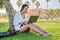 Young woman in headphones with laptop sitting on the grass in the park