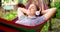 Young woman in headphones listening to music while resting in hammock outdoors