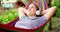 Young woman in headphones listening to music while resting in hammock outdoors