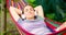 Young woman in headphones listening to music while resting in hammock outdoors