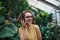 Young woman with headphones standing in greenhouse in botanical garden.