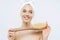 Young woman with healthy fresh skin, uses body brush, smiles gently, wears bath towel on head, poses topless,  over white