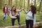 Young woman helping girlfriend step over a fallen tree during a hike with friends in a forest