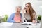 Young woman helping an old senior woman doing paperwork and administrative procedures with laptop computer at home