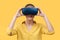 Young woman in her 30s using virtual reality goggles. Woman wearing VR glasses isolated over yellow background. VR experience.