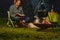 Young woman and her Australian Shepherd outside by a campfire. Reading a book at dusk. Bread, cheese and wine on the