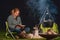 Young woman and her Australian Shepherd outside by a campfire. Reading a book at dusk. Bread, cheese and wine on the